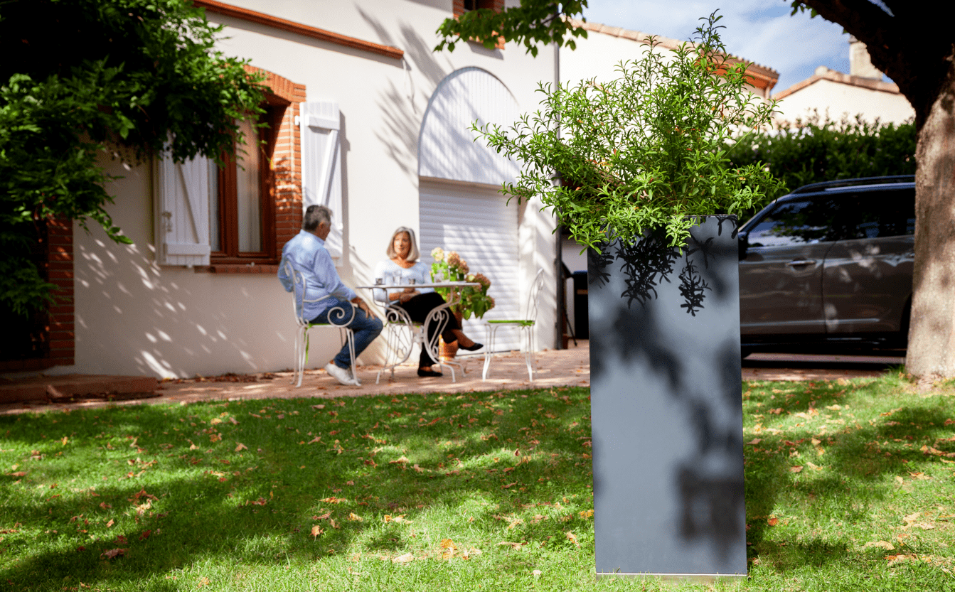 Le piège anti-moustique mis en situation dans le jardin d'un couple qui sont assis en terrasse.