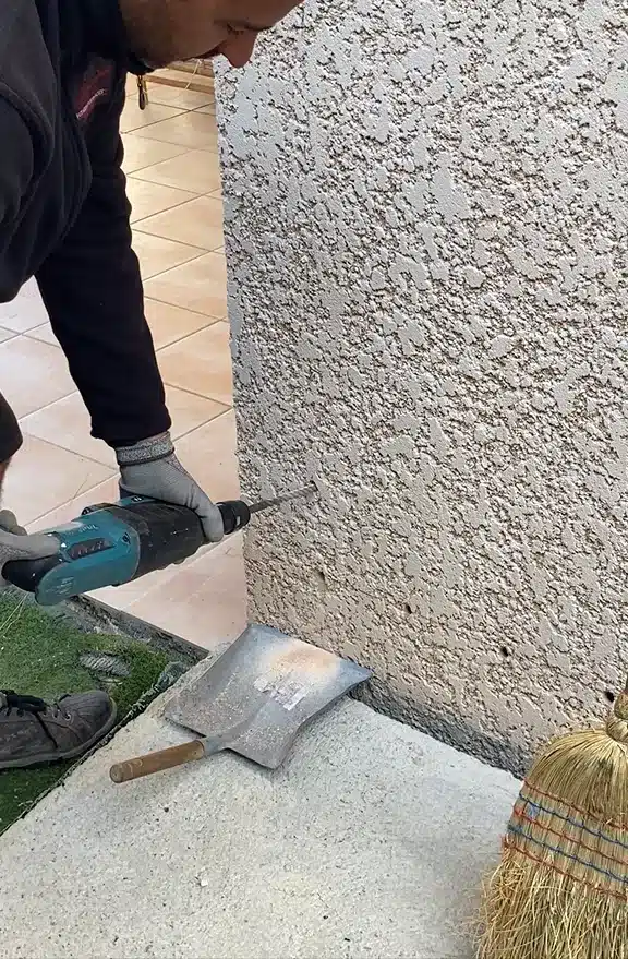 Technicien BST perçant le pied d'une façade crépie pour traiter des remontées capillaires